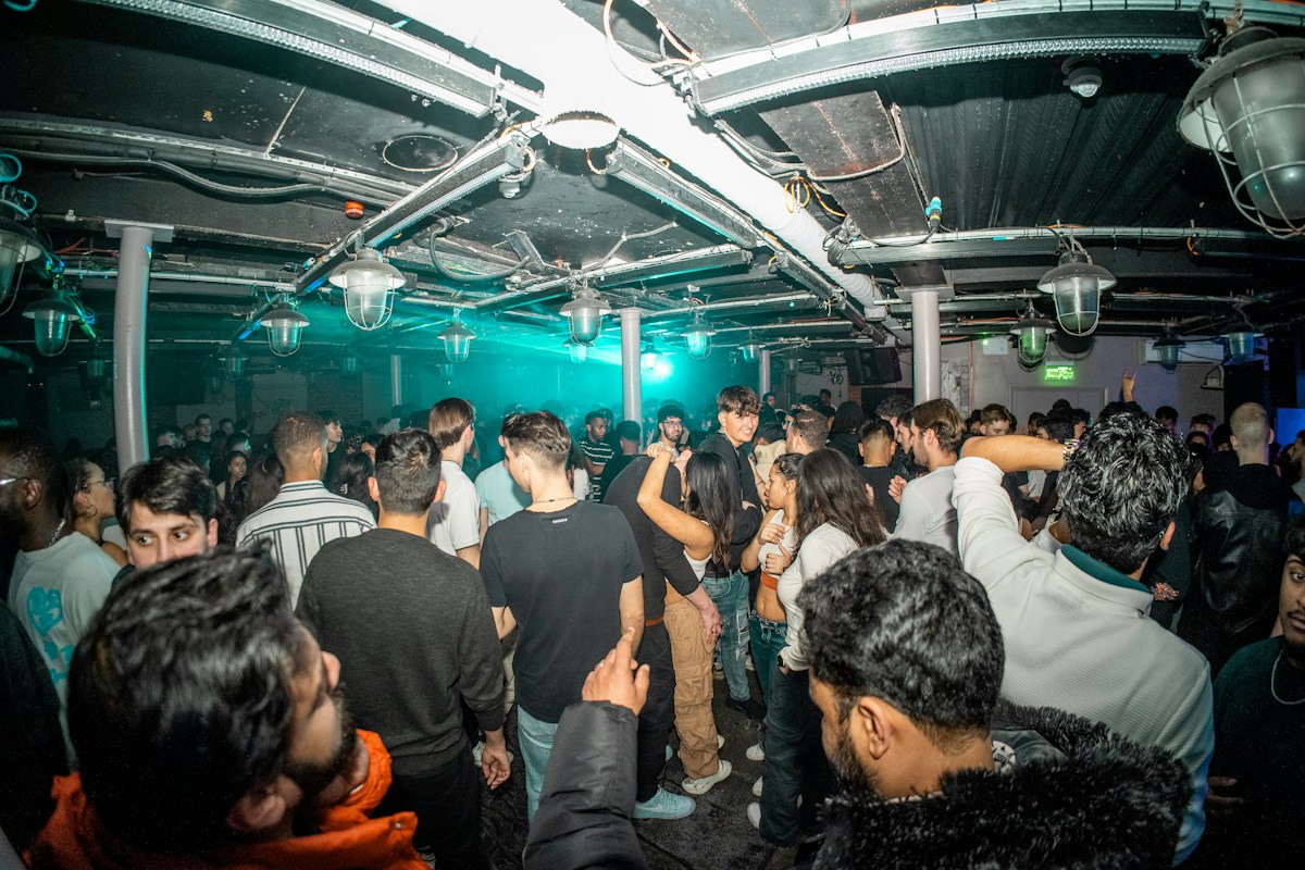 Dancers in an intimate club with a low ceiling and teal lighting